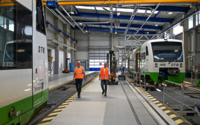 Zwei Menschen in Warnwesten laufen durch eine Zug-Wartungshalle. Zwei Triebwagen der Südthüringenbahn sind zu sehen.